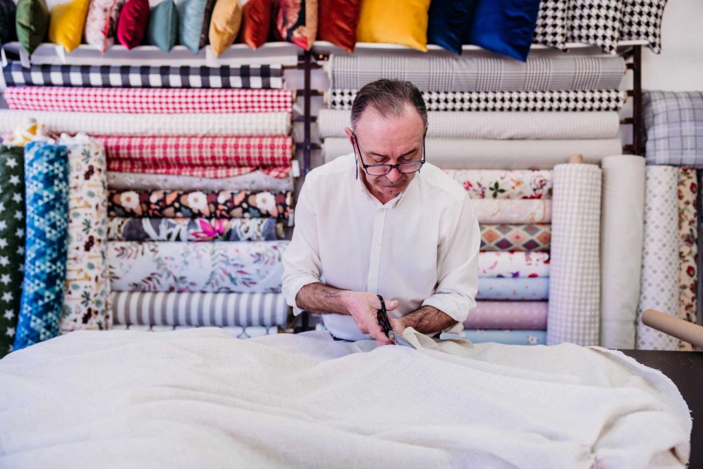 Senior man stitching curtains together | Featured image for the How Are Curtains Made Blog from U Blinds Australia.