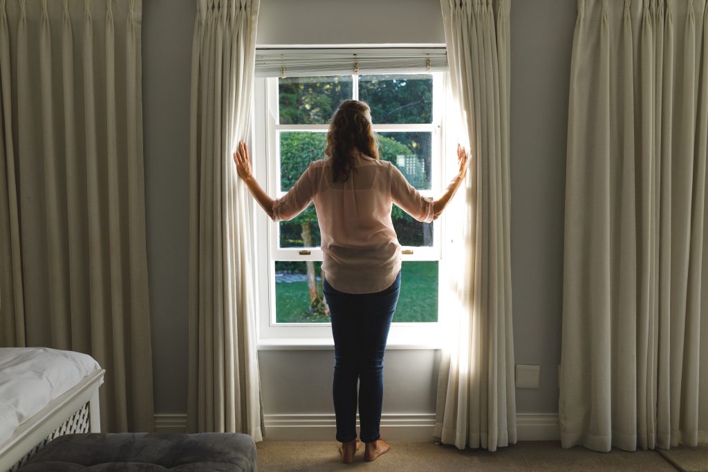 Woman standing in a bedroom window | Featured image for the How to Make a Small Room Look Bigger Blog from U Blinds Australia.