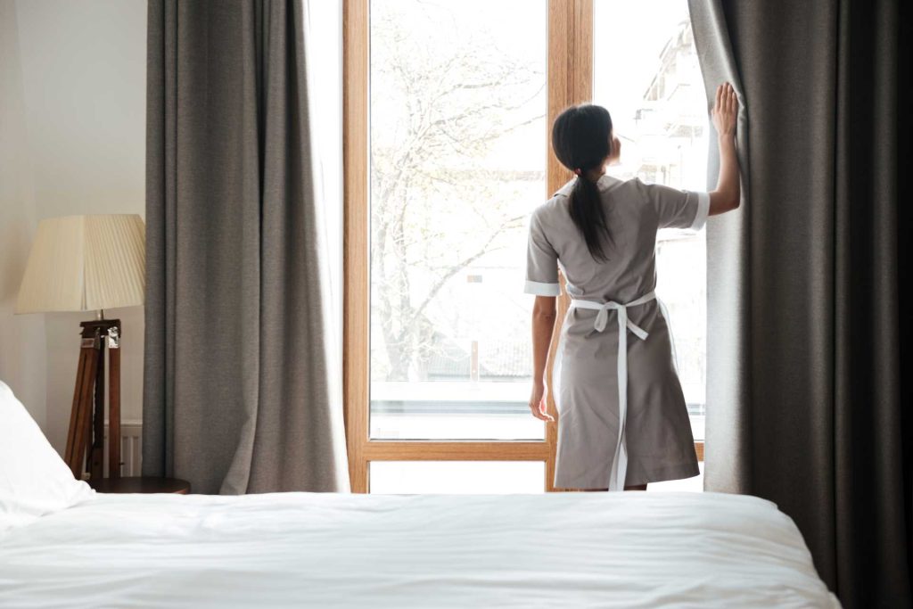 Female housekeeper opening curtains | Featured image for the Best Way to Clean Curtains Blog from U Blinds Australia.