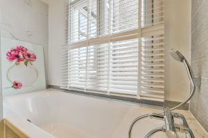 Floral print on the edge of a white bathtub | Featured Image for the Benefits of Shutters for Bathroom Windows blog by U Blinds Australia.