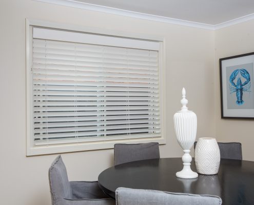 Dining room with white talls, a dark table with a white vase on it and white PVC shutters | Featured Image for the PVC Plantation Shutters Page of U Blinds Australia.